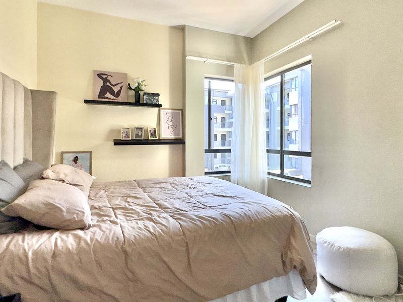 A well-lit bedroom featuring neutral wall tones, large aluminium-framed windows, and a comfortable layout.