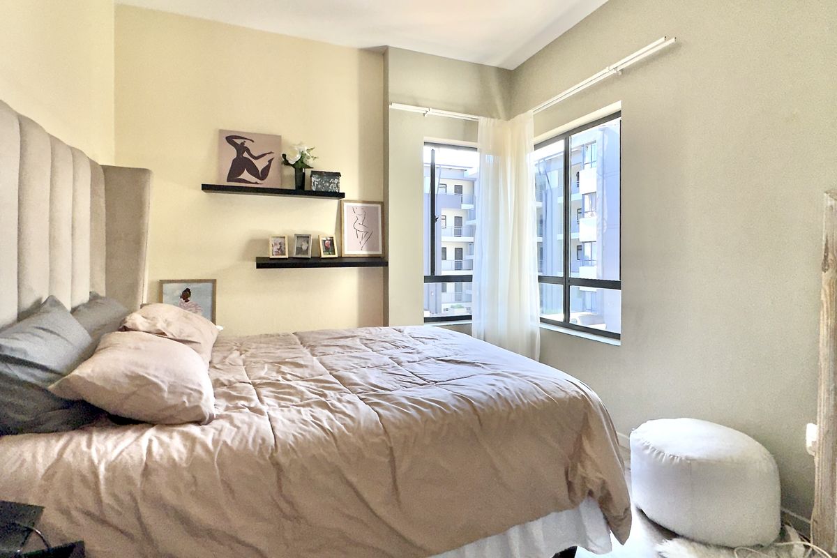 A well-lit bedroom featuring neutral wall tones, large aluminium-framed windows, and a comfortable layout.