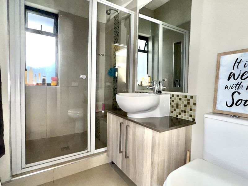 A functional bathroom featuring a glass-enclosed shower, a modern vanity with a vessel sink, mosaic tile accents, and a standard toilet.