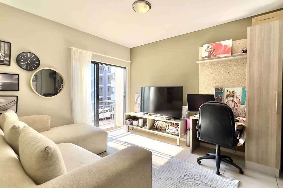 A well-lit living room featuring tiled flooring, a built-in desk area, and a sliding glass door leading to a balcony.