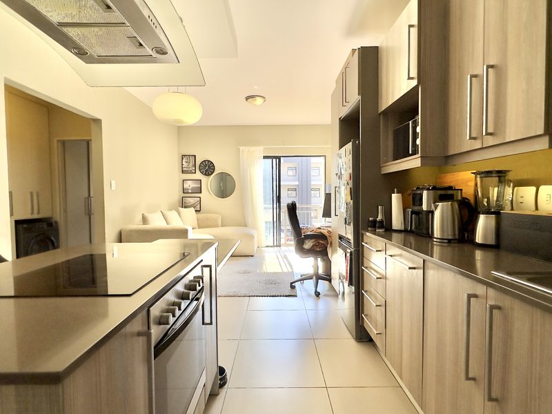 Modern open-plan kitchen and living area featuring sleek cabinetry, stone countertops, integrated appliances, and direct access to a balcony.