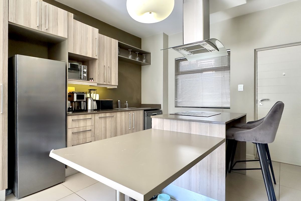 Modern kitchen featuring light wood-grain cabinetry, stone countertops, integrated hob, stainless steel extractor fan, and built-in microwave with tiled flooring.