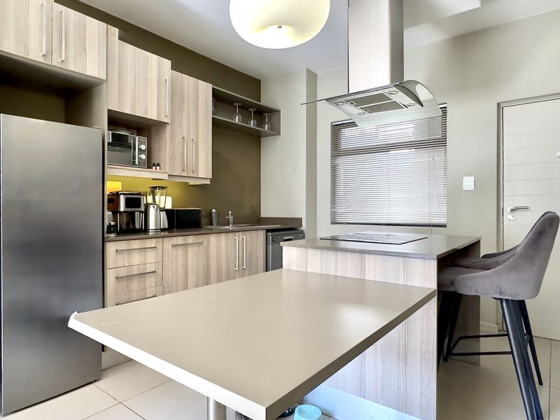 Modern kitchen featuring light wood-grain cabinetry, stone countertops, integrated hob, stainless steel extractor fan, and built-in microwave with tiled flooring.