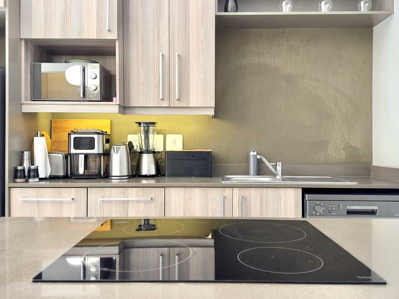 Modern kitchen featuring light wood-grain cabinetry, stone countertops, an integrated electric hob, and under-cabinet lighting for a clean, functional workspace.