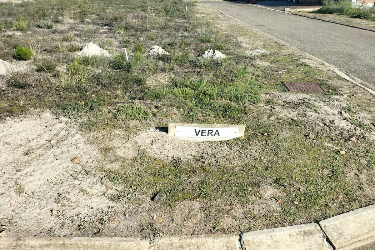 A view of a vacant residential plot featuring a property marker, concrete curbing, and access to a paved street.