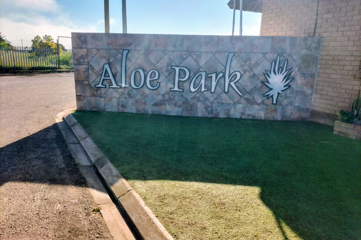 A clear view of the Aloe Park residential estate entrance signage wall, featuring stone cladding and adjacent paved driveway and lawn area.