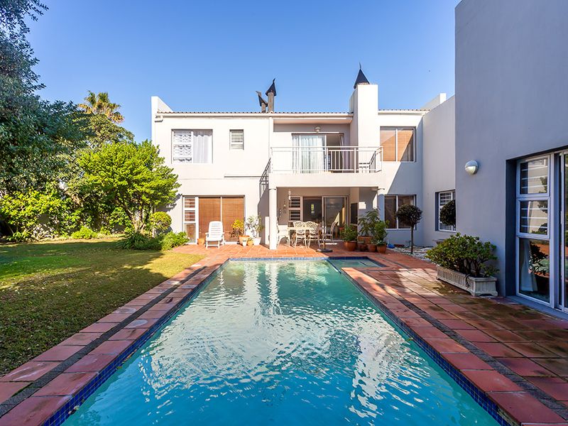 Rear exterior view featuring a swimming pool with terracotta coping, a paved patio area, and a two-story building facade with a balcony.