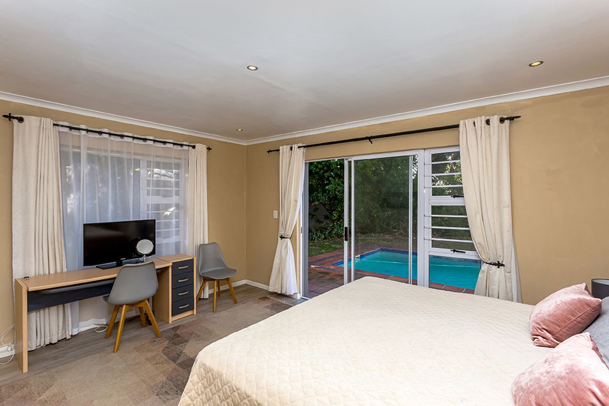 Spacious bedroom featuring laminate flooring, recessed lighting, and sliding glass doors providing direct access to the outdoor pool area.
