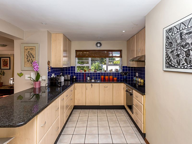 A functional kitchen featuring light wood cabinetry, dark granite countertops, a tiled backsplash, and integrated appliances, offering a clean and practical workspace.