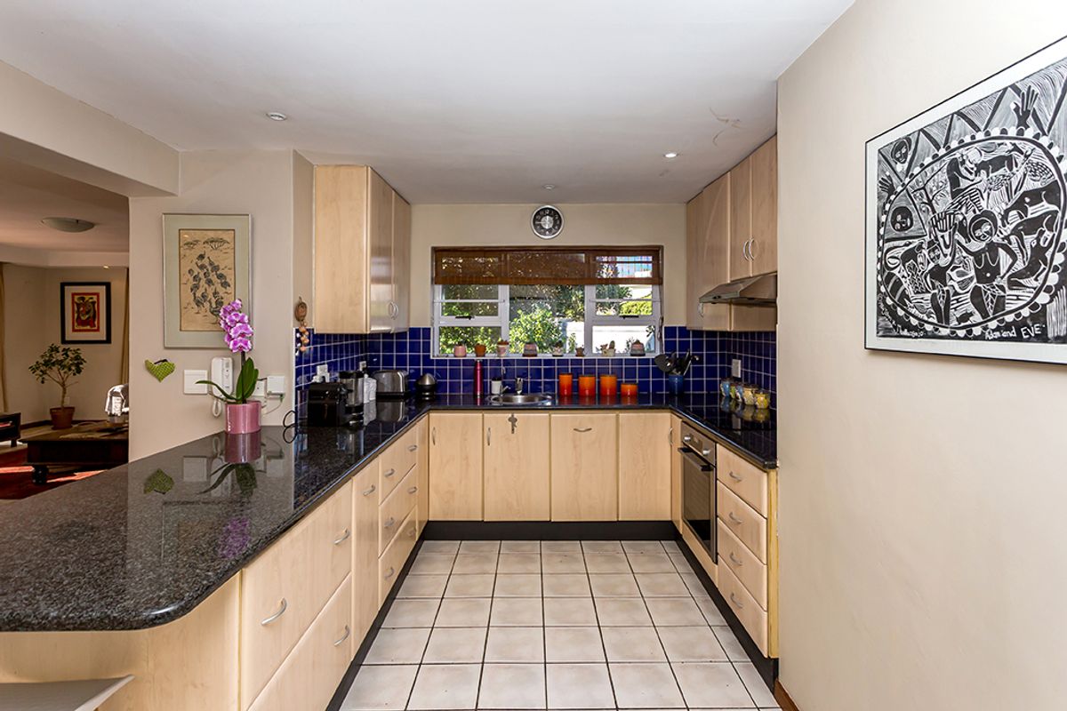 A functional kitchen featuring light wood cabinetry, dark granite countertops, a tiled backsplash, and integrated appliances, offering a clean and practical workspace.