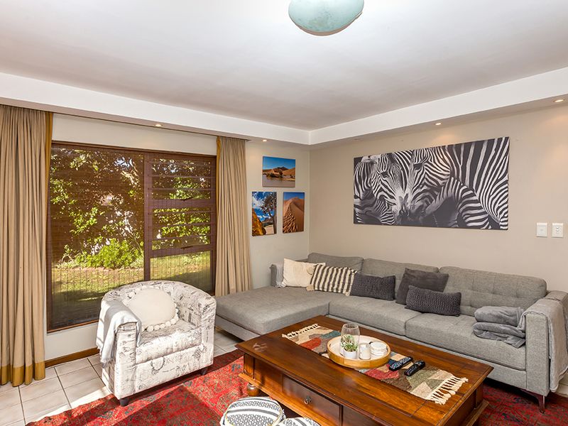 A comfortable living room featuring tiled flooring, recessed ceiling lighting, and a large sliding glass door that provides natural light and garden views.