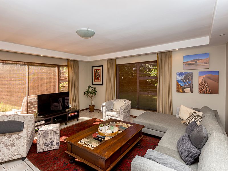 A spacious living room featuring large sliding glass doors, louvre windows, and recessed ceiling lighting, providing ample natural light and access to the outdoors.