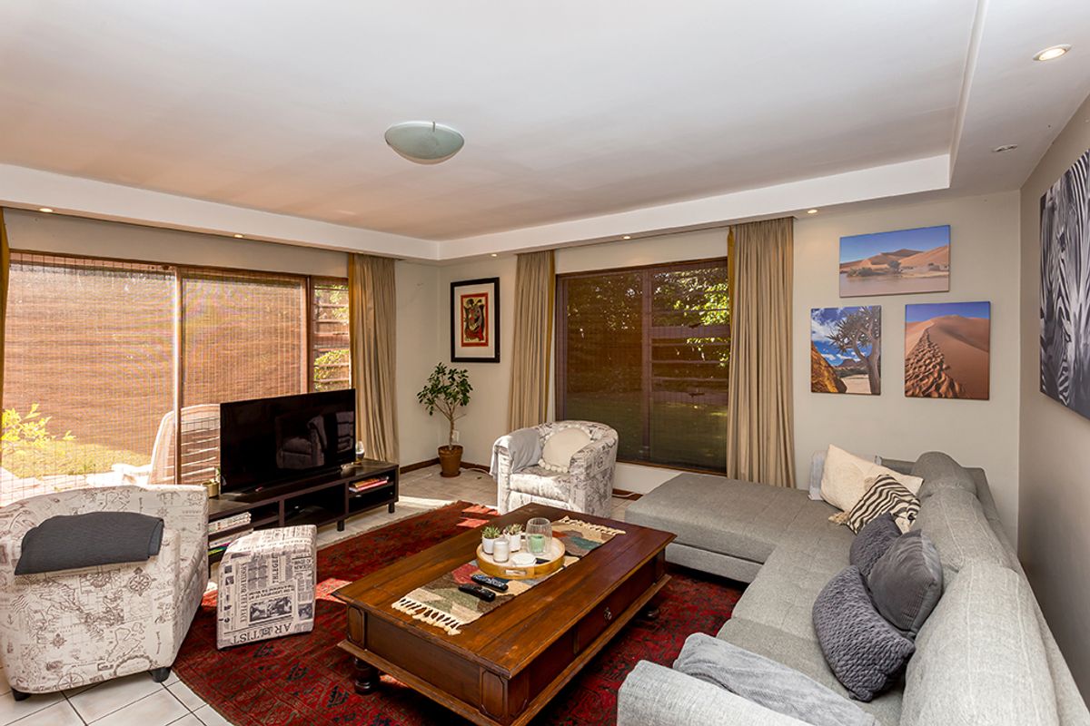 A spacious living room featuring large sliding glass doors, louvre windows, and recessed ceiling lighting, providing ample natural light and access to the outdoors.