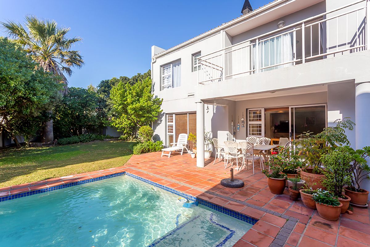 Rear exterior view featuring a swimming pool, terracotta paved patio area, and a balcony overlooking the garden.