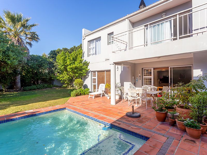 Rear exterior view featuring a swimming pool, terracotta paved patio area, and a balcony overlooking the garden.