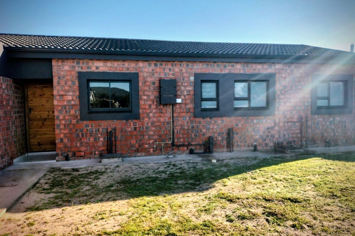 Rear view of a modern house featuring an exposed brick facade, dark window frames, and a tiled roof with a small lawn area.