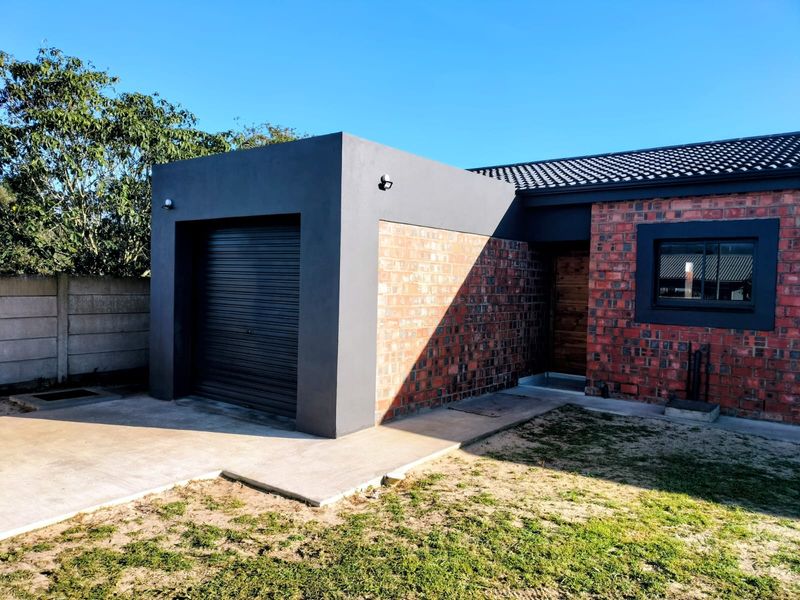 Front view of a modern house featuring a single garage with a roller door, exposed brickwork, and a concrete driveway.