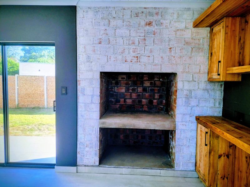 Covered patio area featuring a rustic brick built-in braai, wooden cabinetry, and direct access to the garden through a sliding glass door.