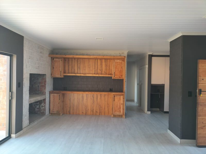 Spacious living area featuring a built-in fireplace, custom timber cabinetry, exposed brick accents, and modern light-toned flooring with direct access to the outdoors.