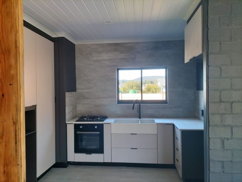 A modern, minimalist kitchen featuring clean cabinetry, a farmhouse sink, gas hob, built-in oven, and stylish stone countertops with a neutral color palette.