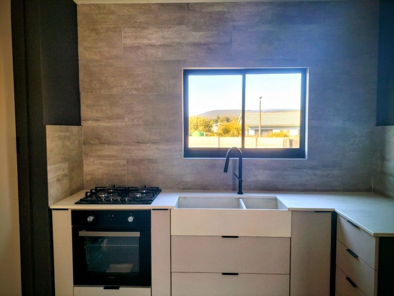 Modern kitchen featuring a built-in oven, gas hob, double basin sink with matte black faucet, and stylish stone-look wall tiling.