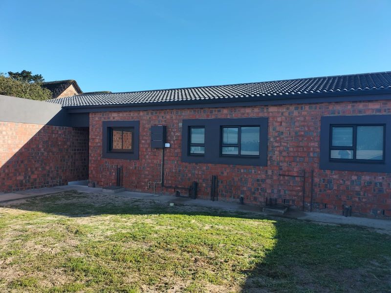 A well-maintained rear exterior view of the house featuring exposed brickwork, dark grey window frames, and a tiled roof.