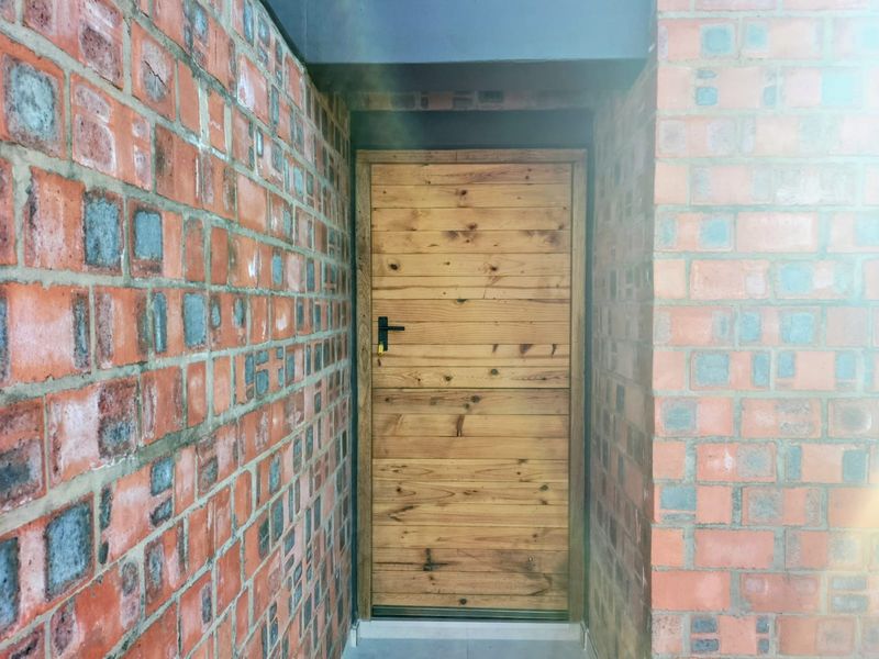 A rustic entrance featuring a natural timber door set within exposed brick walls.