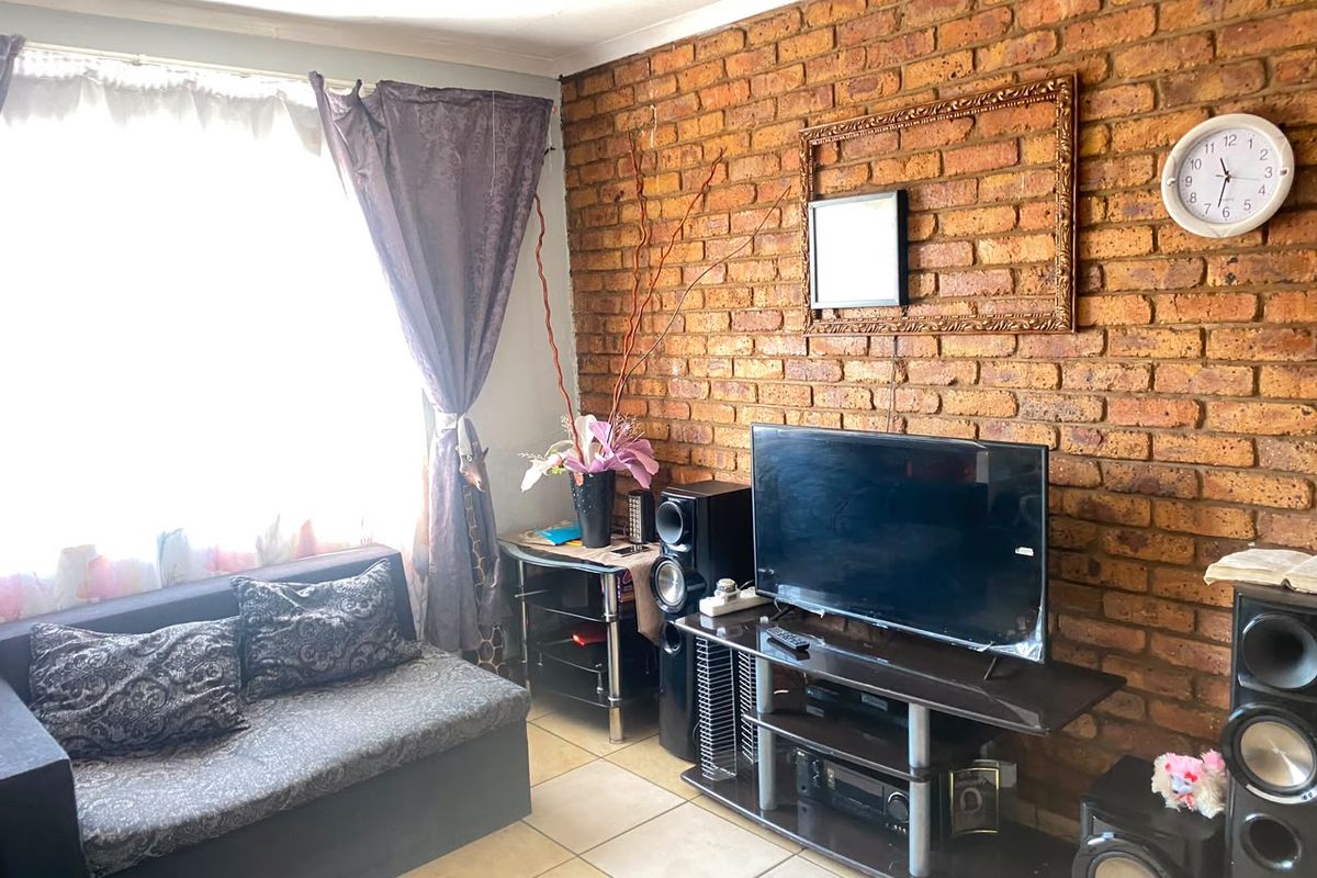 A living room featuring a prominent exposed brick feature wall and neutral ceramic floor tiles, offering a warm and textured aesthetic.