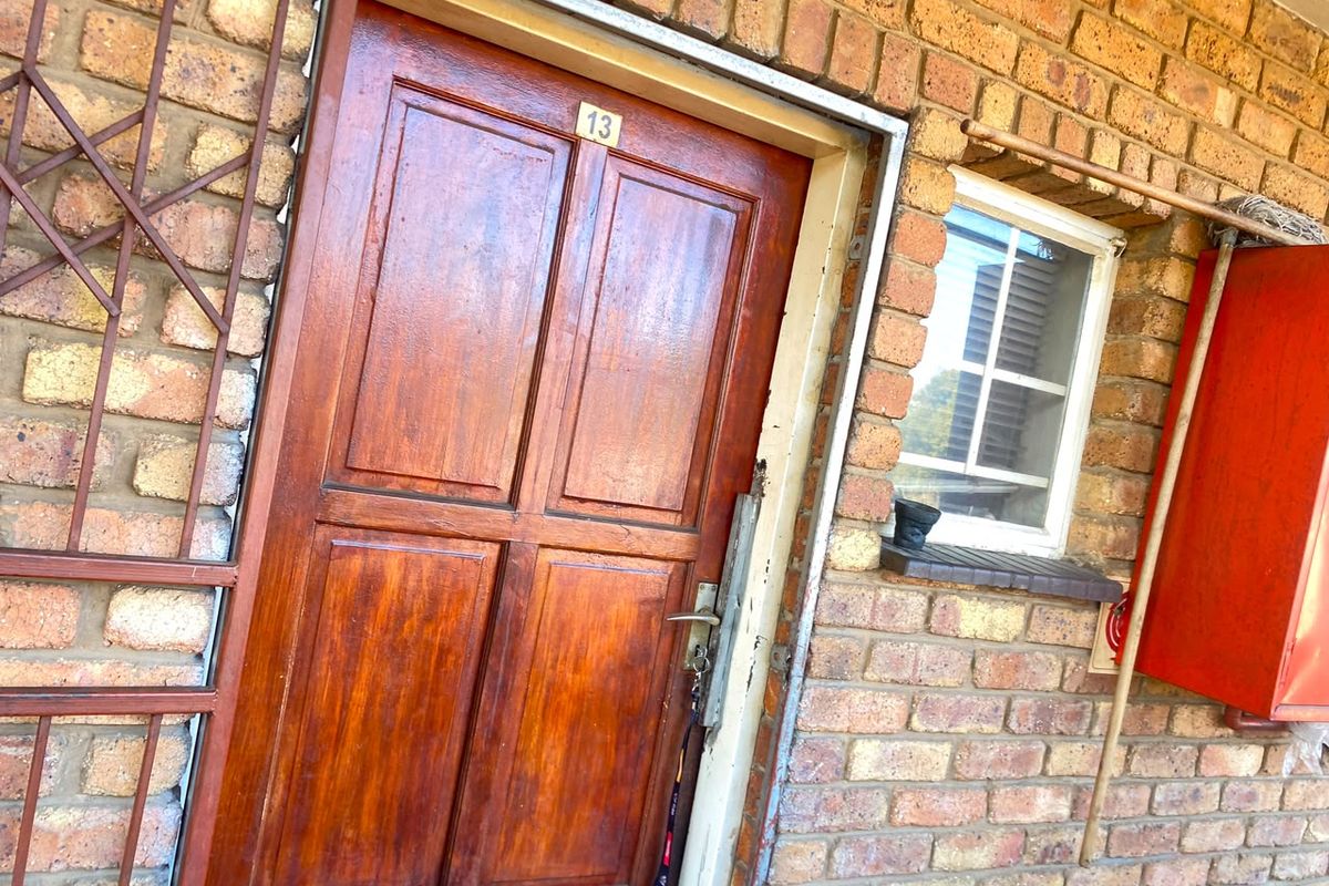 Exterior view of apartment entrance featuring a timber door, security gate, and exposed brickwork facade.