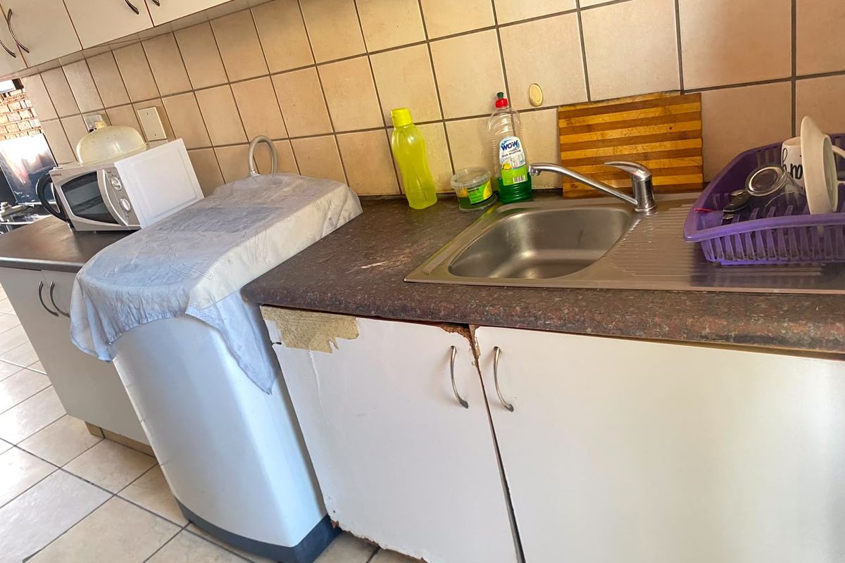 A functional kitchen area featuring a stainless steel sink, tiled backsplash, and laminate countertops with visible wear on the lower cabinetry.