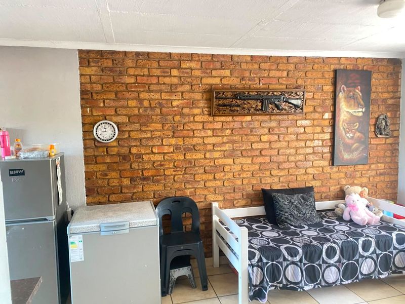 A bedroom featuring an exposed brick feature wall and tiled flooring, providing a rustic aesthetic base for potential interior updates.