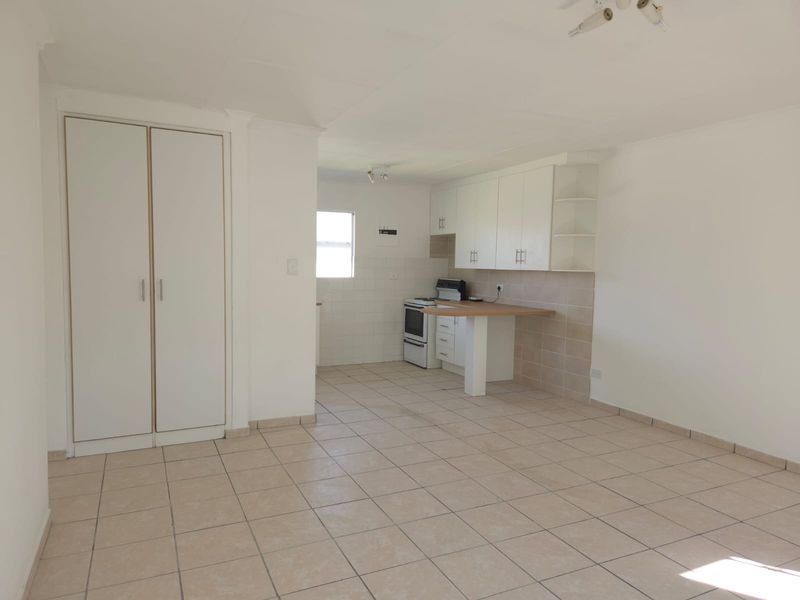 An open-plan living and kitchen area featuring tiled flooring, built-in cupboards, and a functional kitchen layout with a breakfast counter.