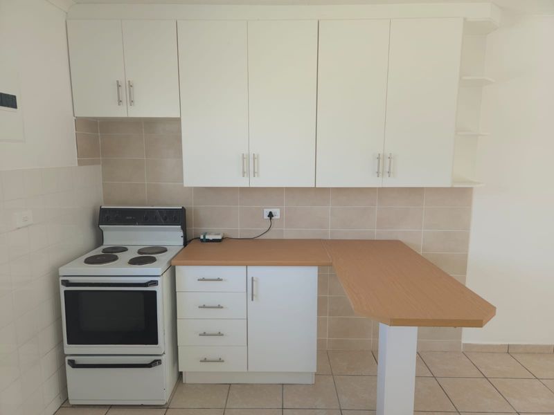 A clean, functional kitchen featuring white cabinetry, a laminate breakfast bar, ceramic tile backsplash, and a freestanding electric stove.