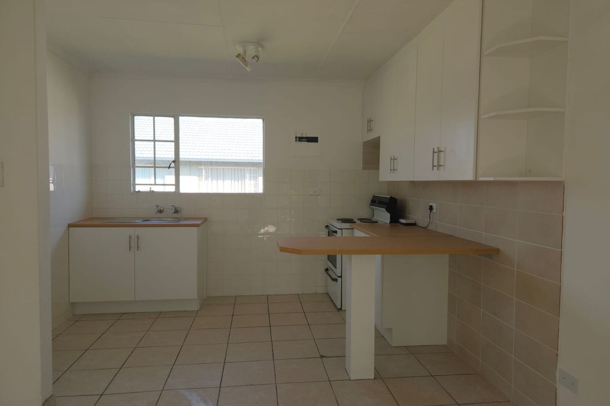 A functional kitchen featuring white cabinetry, tiled splashbacks, tiled flooring, and a breakfast bar, offering a clean and practical workspace.