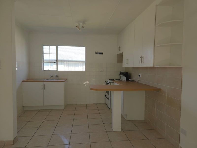 A functional kitchen featuring white cabinetry, tiled splashbacks, tiled flooring, and a breakfast bar, offering a clean and practical workspace.
