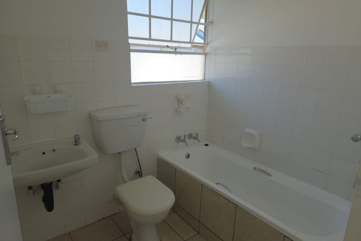 A functional bathroom featuring a built-in bathtub, wall-mounted basin, and toilet, finished with white wall tiles and neutral floor tiling.
