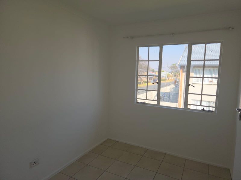 A bright, empty bedroom featuring neutral tiled flooring and a window with security bars, offering a clean canvas for personalization.