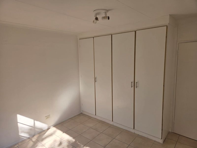 A bright, empty bedroom featuring neutral tiled flooring and floor-to-ceiling built-in cupboards, offering a clean canvas for personalization.