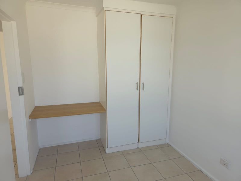 A clean, empty bedroom featuring a built-in wardrobe and a fixed desk area with neutral tiled flooring.