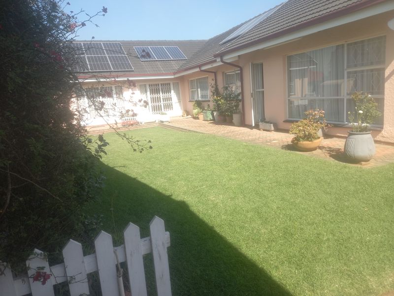 A well-maintained rear garden featuring a brick-paved patio area, lush lawn, and solar panels installed on the tiled roof.