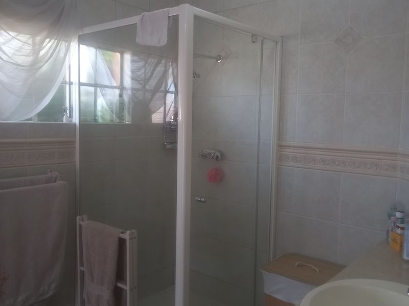 A functional bathroom featuring a glass shower enclosure, tiled walls with decorative border, and a basin.