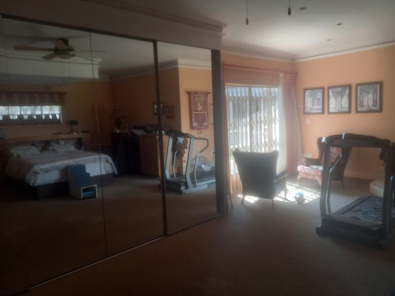 Spacious bedroom featuring large mirrored sliding wardrobes, ceiling fan, and direct access to the exterior through a security gate.