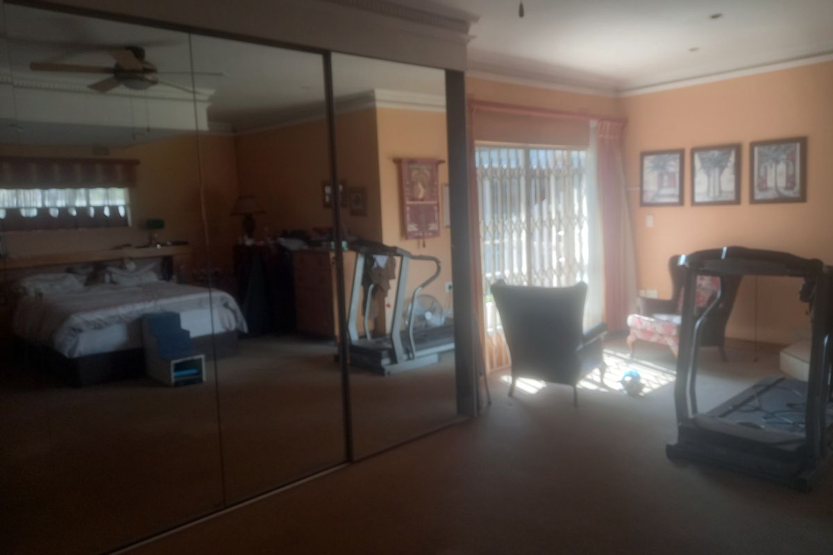 Spacious bedroom featuring large mirrored sliding wardrobes, ceiling fan, and direct access to the exterior through a security gate.