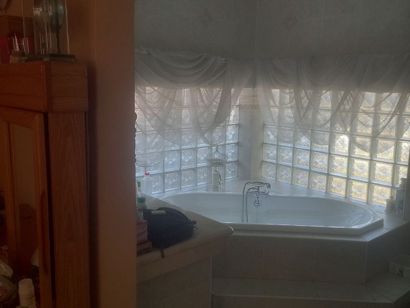 A bathroom featuring a built-in corner bathtub surrounded by glass block windows and tiled flooring, accessed through a decorative archway.