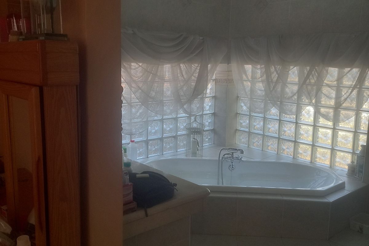 A bathroom featuring a built-in corner bathtub surrounded by glass block windows and tiled flooring, accessed through a decorative archway.