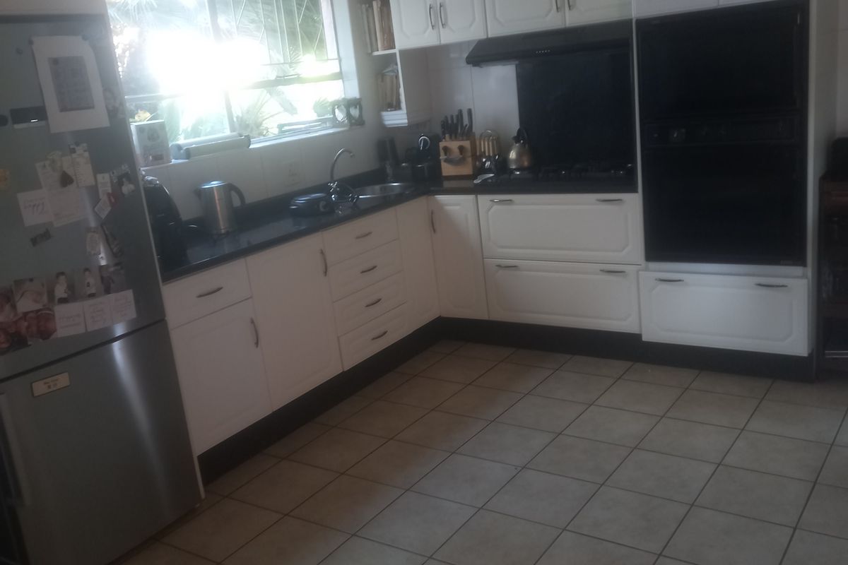 A functional kitchen featuring white cabinetry, dark countertops, a built-in double oven, and tiled flooring with natural light from the window.