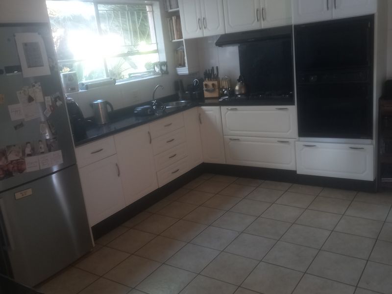 A functional kitchen featuring white cabinetry, dark countertops, a built-in double oven, and tiled flooring with natural light from the window.