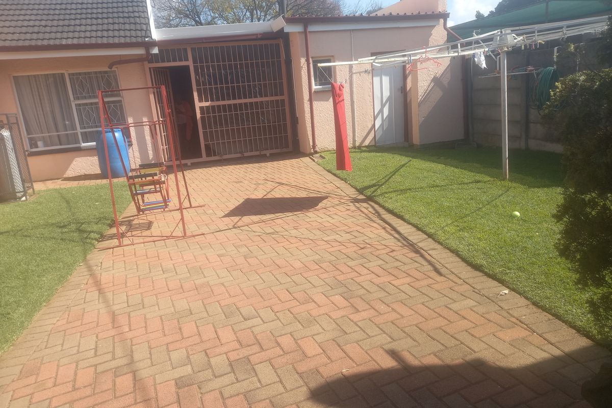 A rear exterior view featuring a paved patio area, a small lawn, and a secure entrance with metal security gates.