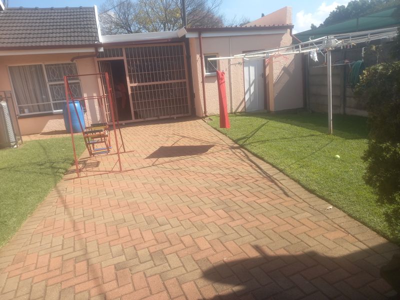 A rear exterior view featuring a paved patio area, a small lawn, and a secure entrance with metal security gates.