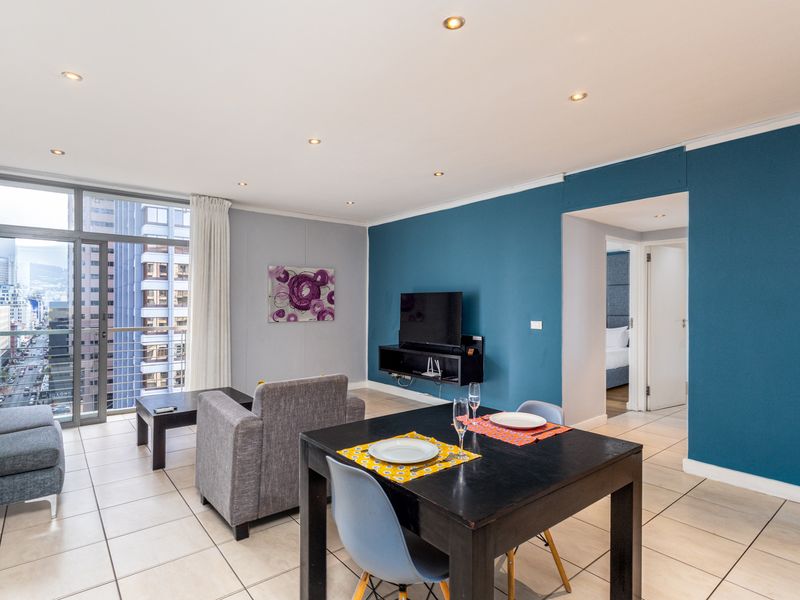 Open-plan living and dining area featuring tiled floors, recessed lighting, and a sliding glass door leading to a balcony with city views.
